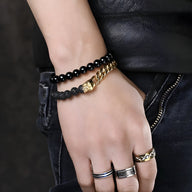 Bracelet en acier inoxydable argenté avec perles noires volcaniques et double tête de mort dorée.