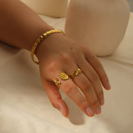 Bracelet jonc en acier inoxydable plaqué or avec motif texturé porté au poignet féminin.