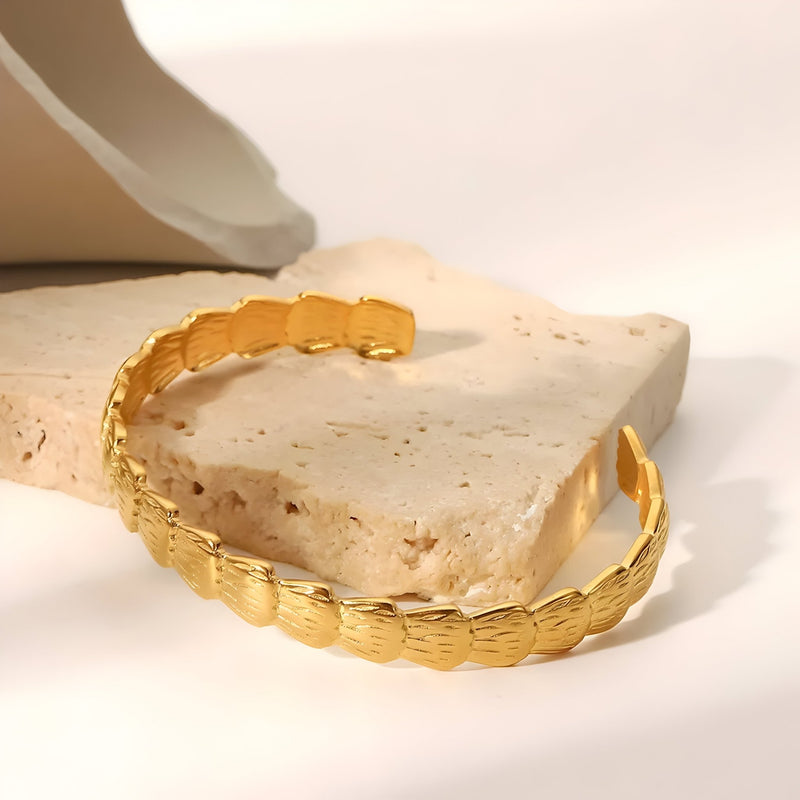 Bracelet jonc en acier inoxydable plaqué or avec motifs ovales texturés, finition brillante.