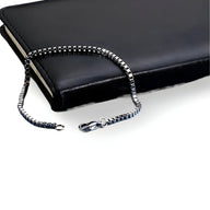 Bracelet pour homme en acier inoxydable argenté à maille vénitienne avec fermoir mousqueton, posé sur un carnet noir.