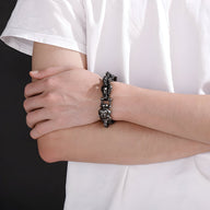Bracelet en acier inoxydable gris avec têtes de mort et tête de chien, porté au poignet.