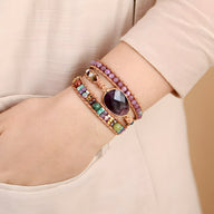 Bracelet multi-rangs en améthyste violette, jaspe multicolore et perles dorées sur poignet féminin.