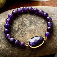 Bracelet pour femme en perles d'améthyste violettes avec un pendentif ovale facetté bordé d'or.