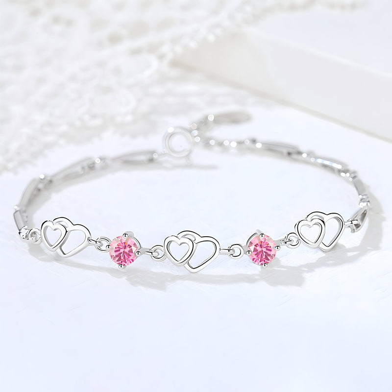 Bracelet en argent massif avec charms cœurs entrelacés et cristaux roses étincelants, style délicat.