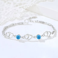 Bracelet en argent massif avec trois charms cœurs et deux pierres bleues scintillantes.
