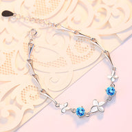 Bracelet en argent avec pendentifs trèfle à quatre feuilles et pierres bleues scintillantes.
