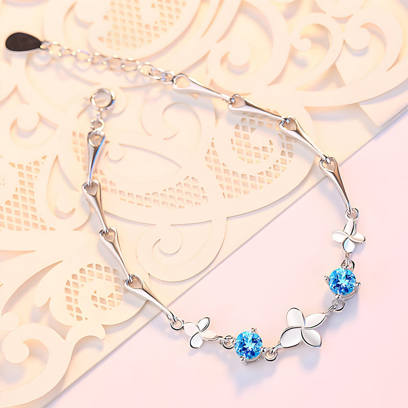 Bracelet en argent avec pendentifs trèfle à quatre feuilles et pierres bleues scintillantes.