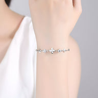 Bracelet en argent massif avec pendentif trèfle à quatre feuilles et petits strass sur poignet féminin.