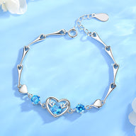 Bracelet en argent avec charms cœur et cristaux bleus, design délicat et élégant pour femme.
