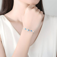 Bracelet en argent avec charms cœur et perles bleues porté au poignet féminin.