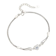 Bracelet argent sterling pour femme avec chaîne fine, ailes d'ange et cœur central orné d'un petit cristal bleu.