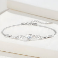 Bracelet fin en argent sterling avec un cœur central orné d’un cristal, ailes d’ange délicates de chaque côté.