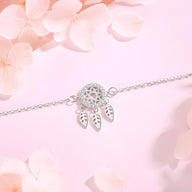 Bracelet en argent sterling avec pendentif attrape-rêves et trois plumes délicates sur fond rose pâle.