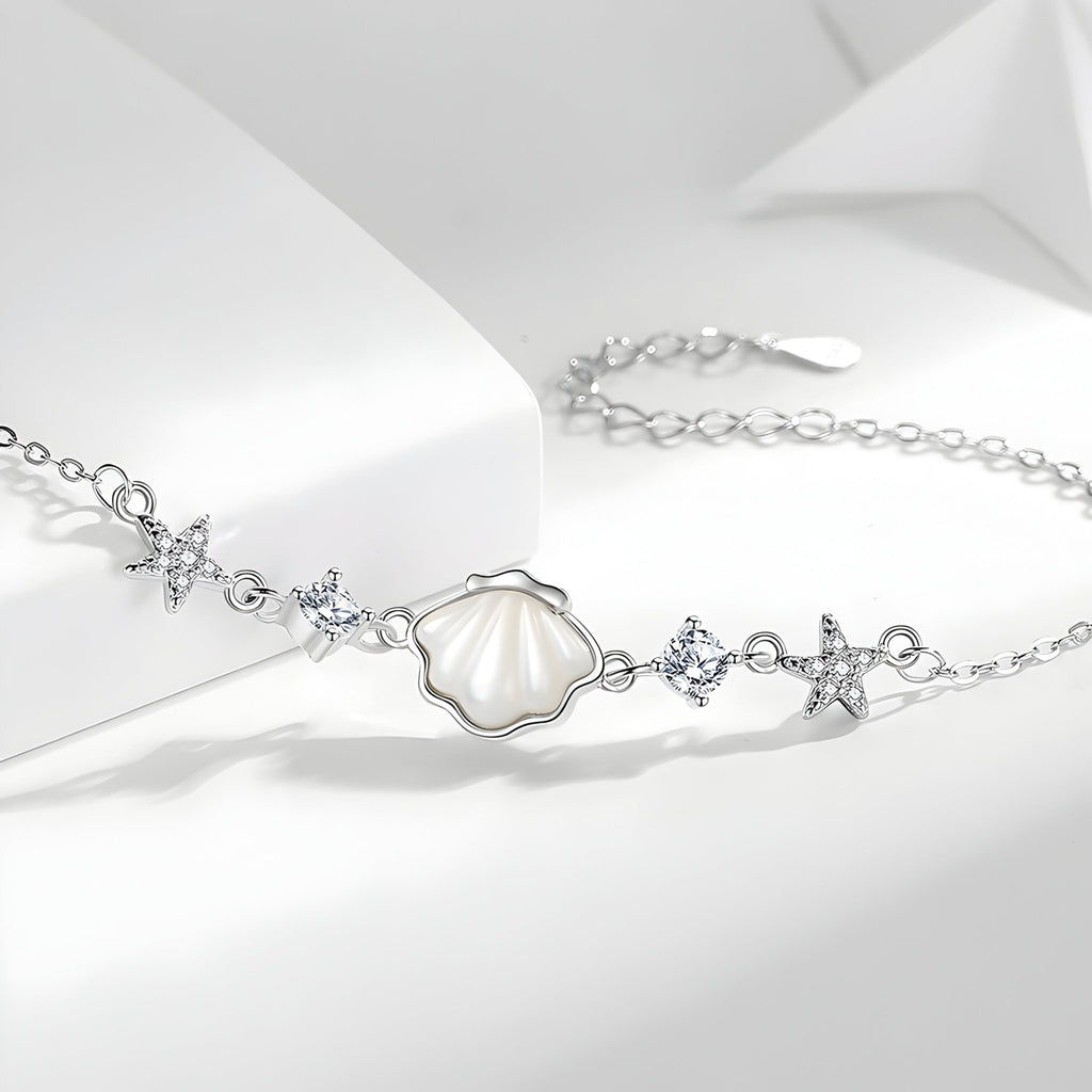 Bracelet en argent sterling avec pendentifs coquillage nacré et étoiles de mer, détails cristaux transparents.