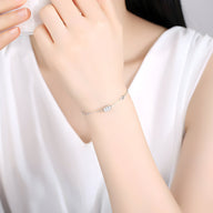 Bracelet en argent sterling fin avec charm cylindrique minimaliste, porté sur poignet féminin.