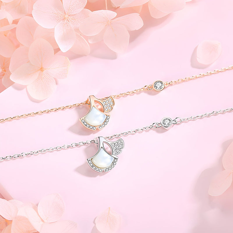 Bracelet en argent avec charm feuille de ginkgo blanc orné de petits cristaux sur fond rose pâle.