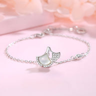 Bracelet fin en argent sterling avec pendentifs feuilles de ginkgo délicats et chaîne à maillons sur fond rose pâle.