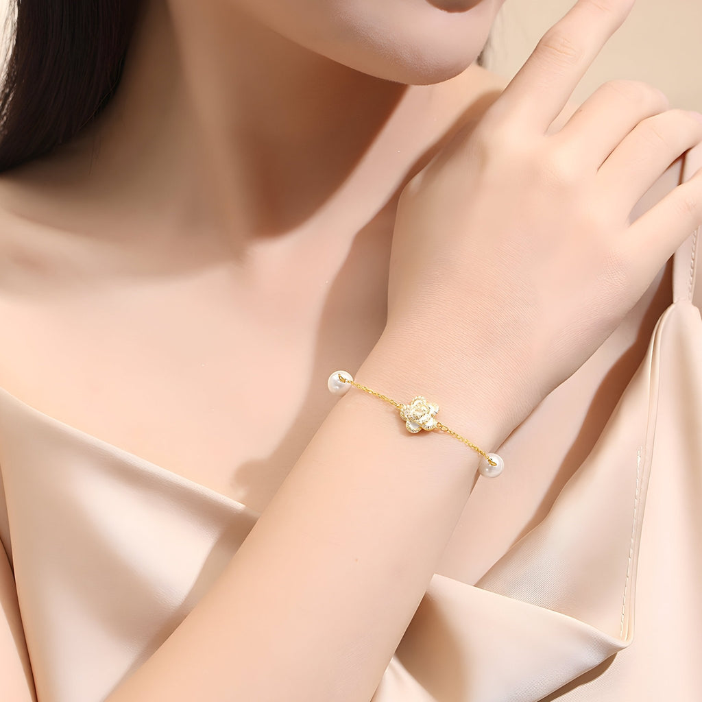 Bracelet en argent sterling doré avec charm floral et perles sur poignet féminin.