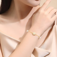 Bracelet en argent sterling doré avec charm floral et perles sur poignet féminin.