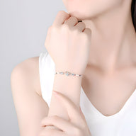 Bracelet fin en argent sterling avec cœur central orné de petites pierres brillantes, porté au poignet.