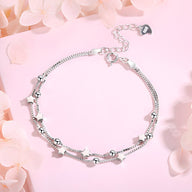 Bracelet fin en argent sterling avec petits charms étoiles et chaînes délicates sur fond rose pâle.
