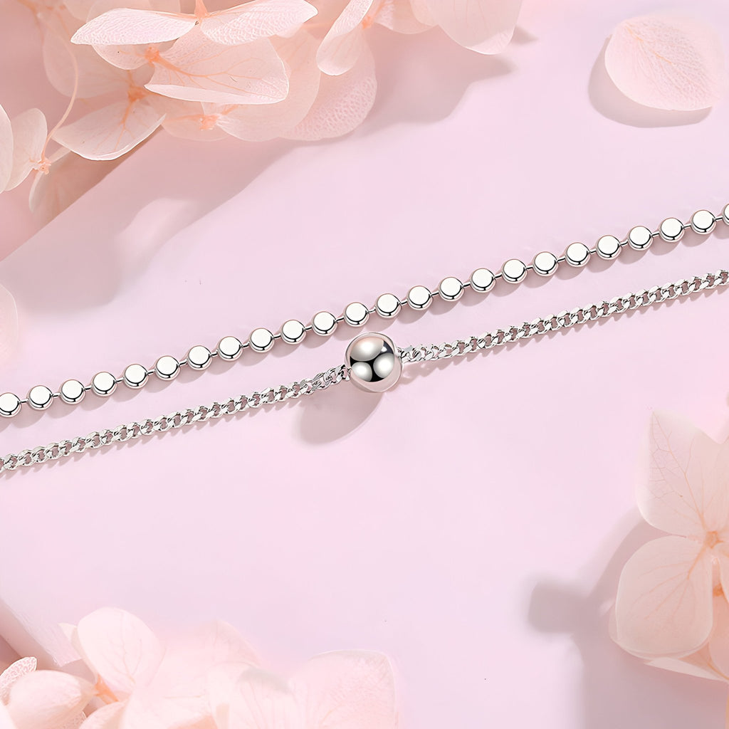 Bracelet double maille en argent sterling avec perle centrale lisse sur fond rose pâle.