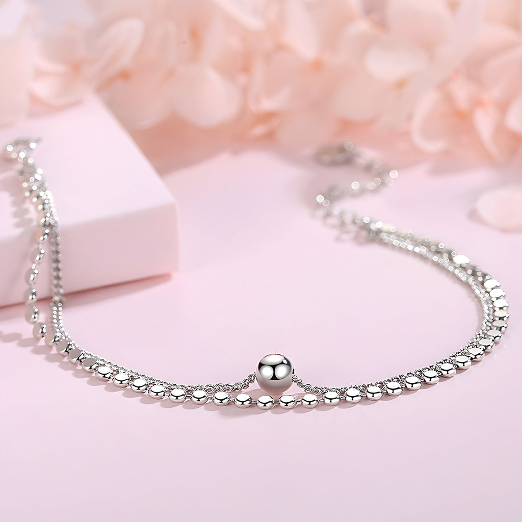 Bracelet en argent sterling double maille avec perle centrale brillante sur fond rose pâle.