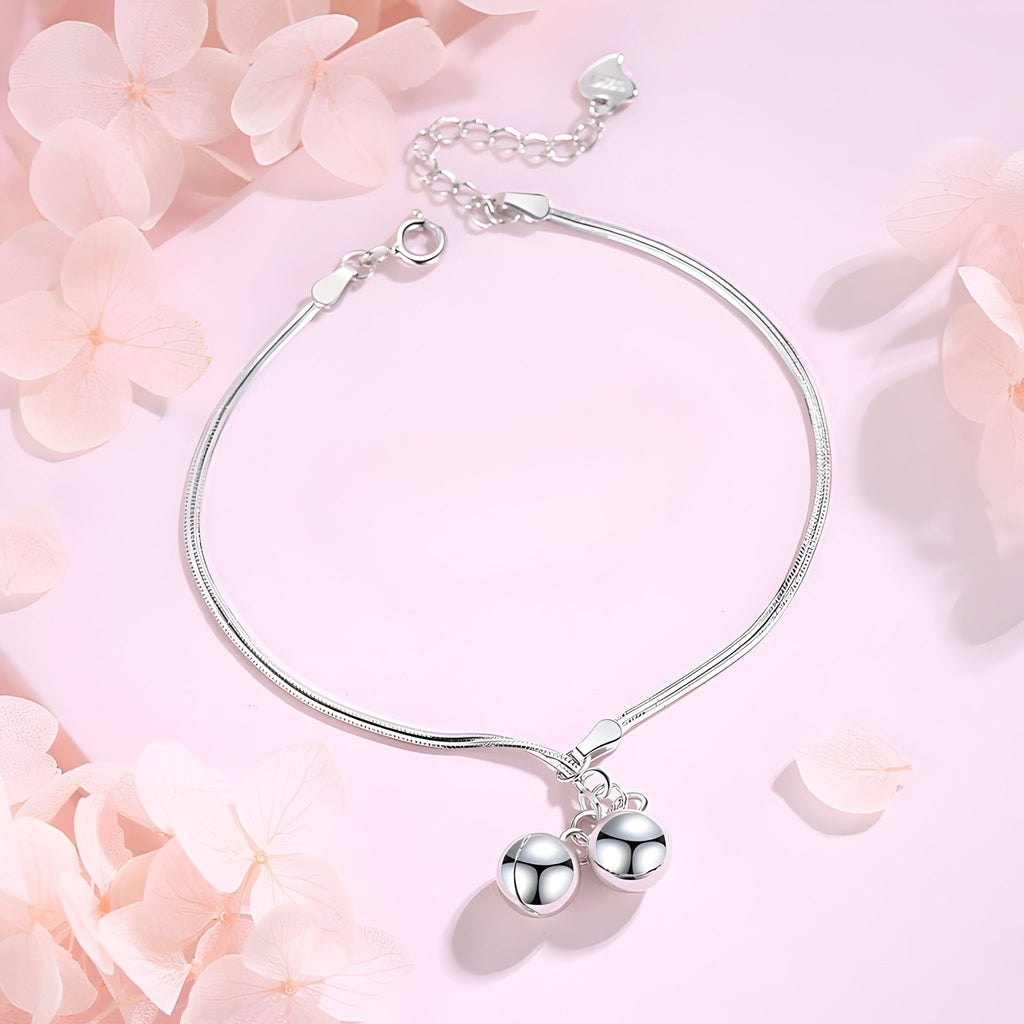 Bracelet fin en argent sterling avec deux perles lisses suspendues sur fond rose pâle.