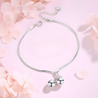 Bracelet fin en argent sterling avec deux perles lisses suspendues sur fond rose pâle.