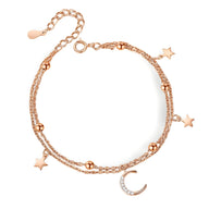 Bracelet en or rosé avec chaîne double, perles, lune et étoiles scintillantes en pendentifs.
