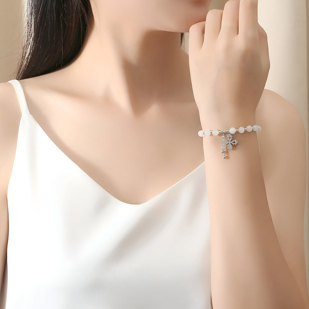 Bracelet argent sterling avec perles blanches et charms jade et trèfle porté au poignet.