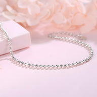 Bracelet femme en argent sterling composé de petites perles rondes lisses, modèle Erika, sur fond rose pâle.