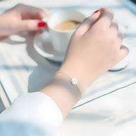 Bracelet fin en argent sterling avec pendentif smiley rond porté au poignet féminin avec vernis rouge.