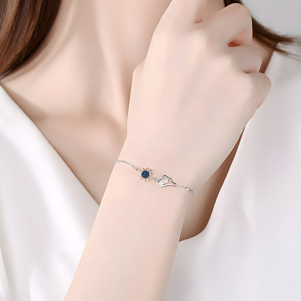 Bracelet fin en argent sterling avec pendentif soleil noir et nuage délicat, porté au poignet.