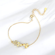 Bracelet doré fin avec pendentifs trèfle à trois feuilles sertis de petites pierres brillantes.