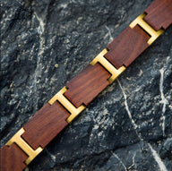 Bracelet en bois d'acajou marron avec entretoises métalliques dorées, design moderne et épuré.