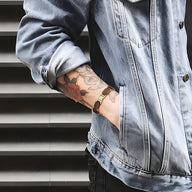 Bracelet en bois d'acajou marron avec détails argent portés sur poignet tatoué, style décontracté.