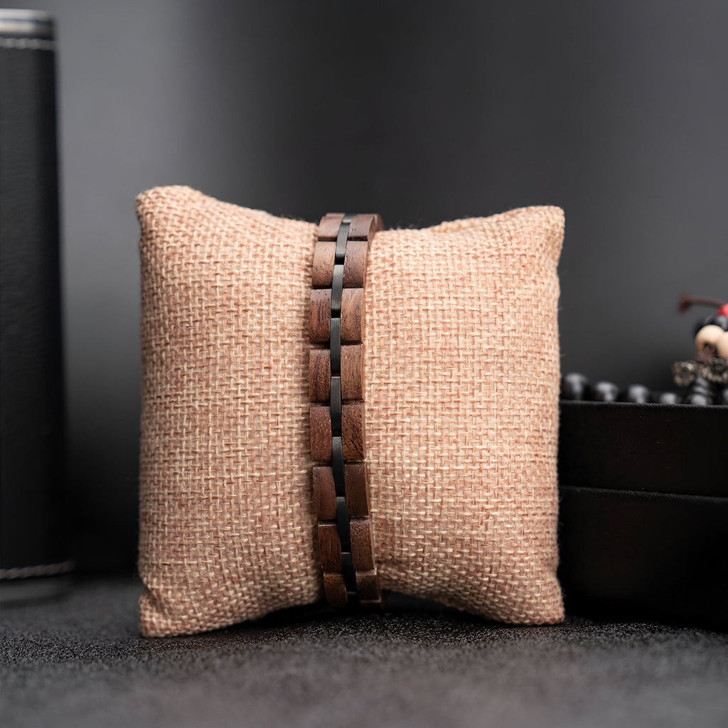 Bracelet pour homme en bois de noyer marron avec maillons larges et finition lisse posé sur coussin beige textured.