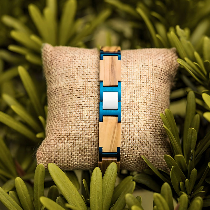 Bracelet en bois d'olivier beige avec inserts bleus, design masculin moderne, posé sur coussin en toile nature.