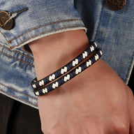 Bracelet en cuir bleu tressé avec motifs blancs porté sur poignet, style double tour.
