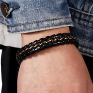 Bracelet en cuir noir tressé avec détails ondulés et liens argentés portés avec une veste en jean.