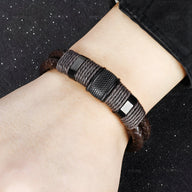 Bracelet en cuir marron avec cordelettes enroulées noires et fermeture métallique carrée.