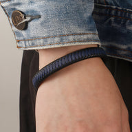 Bracelet en cuir bi-colore bleu et noir tressé, modèle Loïc, porté au poignet masculin sous une veste en jean.