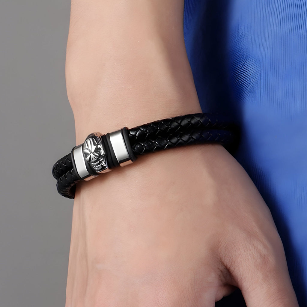 Bracelet double en cuir tressé noir avec tête de mort argentée et fermoir métallique.