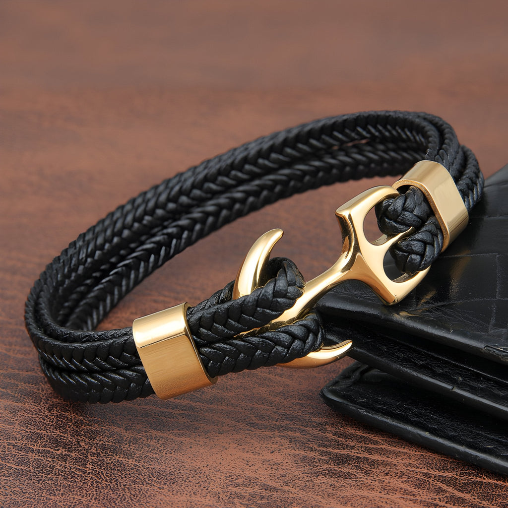 Bracelet en cuir noir tressé avec motif ancre dorée et fermoir assorti, style marin élégant.