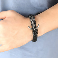 Bracelet en cuir noir avec motif ancre entrelacée en métal sur poignet homme.