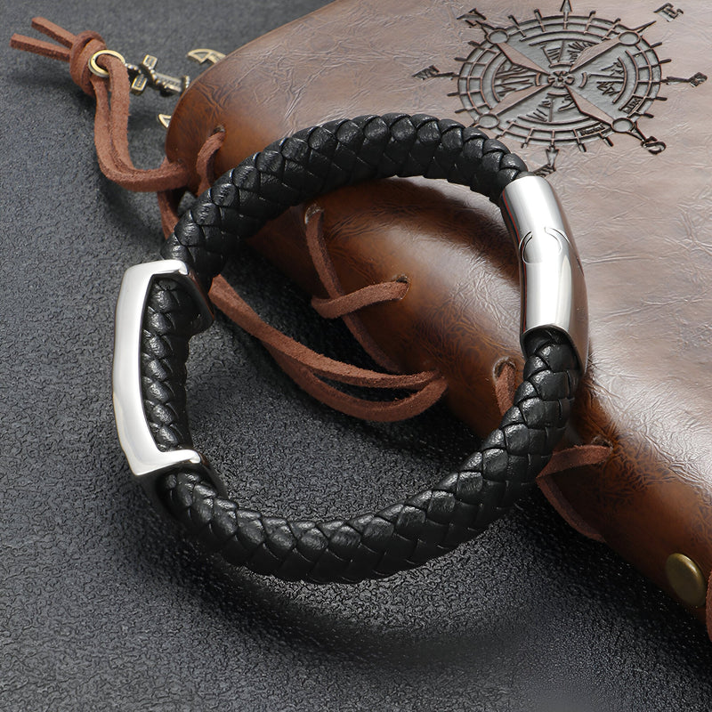 Bracelet pour homme en cuir noir tressé avec fermoir argenté et motif tête de mort ailée.