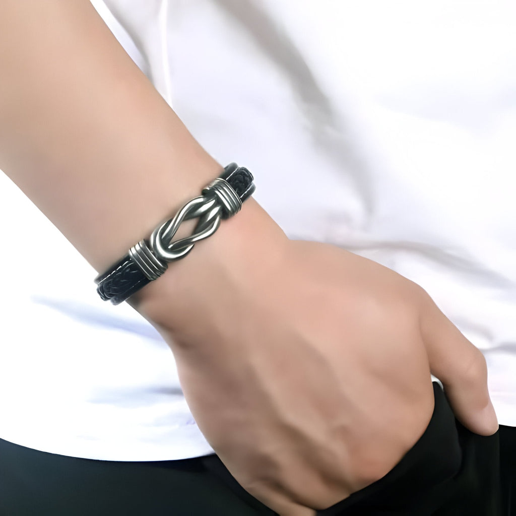 Bracelet en cuir noir tressé avec fermoir en métal argenté porté au poignet.