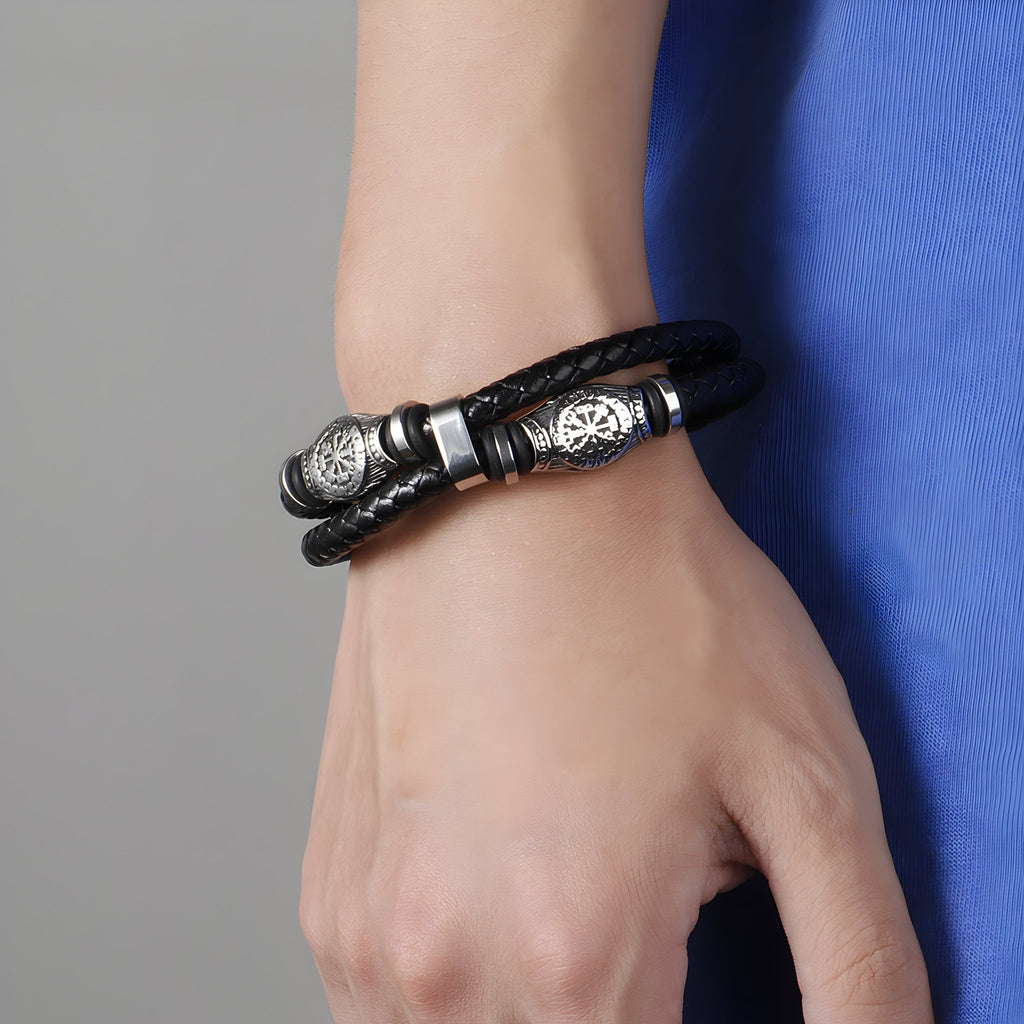 Bracelet en cuir noir tressé avec motifs vikings en métal argenté porté au poignet.