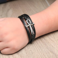 Bracelet multi-rangs en cuir noir avec motif croix argentée, style Benjamin, porté au poignet.